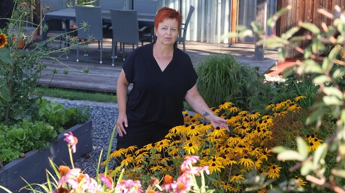 Zu sehen ist eine Frau mit kurzen roten Haaren inmitten ihrer Blumen 