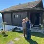Ein Pensionistenpaar steht vor einem Holzhaus auf einem Berg
