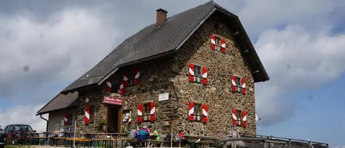 Ein typisches Steinhaus mit roten und weißen Balken, davor sitzen Gäste