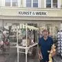 Ein Mann hält eine selbstgemachte Pfeffermühle und einen selbstgemachten Pinocchio in den Händen. Er steht vor einem Geschäft und lächelt in die Kamera.