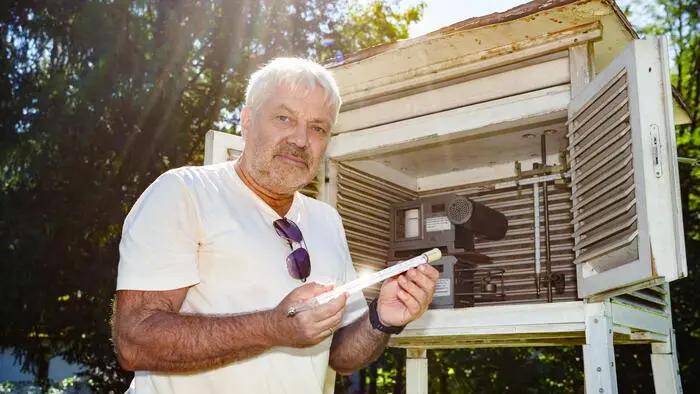 Der Forscher Ulrich Foelsche steht vor seiner Wetterstation und hält ein Thermometer in der Hand.