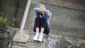 Sujetfoto einer Frau auf einer Mauer. Sie bedeckt ihre Gesicht mit einer Hand und zeigt mit der anderen „Stopp“