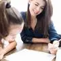 Beautiful female teacher smiling while teaching girl at home