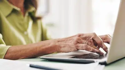 Blick auf einen Laptop, wo eine Frau gerade darauf tippt