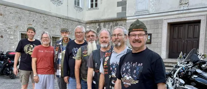 Mehrere Männer haben sich neben Motorrädern für ein Gruppenfoto aufgestellt. Manche tragen Biker-Kleidung