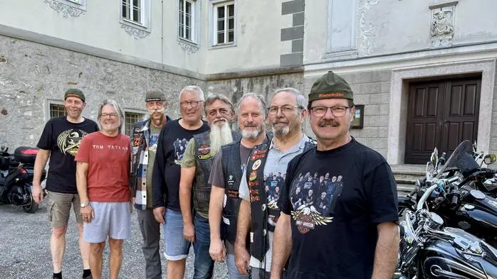 Mehrere Männer haben sich neben Motorrädern für ein Gruppenfoto aufgestellt. Manche tragen Biker-Kleidung
