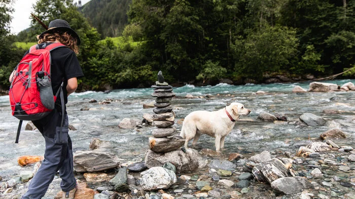 Eine Frau wandert mit einem Hund entlang der Isel in Osttirol
