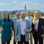 Gruppenfoto mit drei Männern und zwei Frauen auf einer Brücke, im Hintergrund ist eine Stadt mit Kirchturm zu sehen