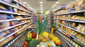 Ein Einkaufswagerl fährt zwischen vollen Supermarktregalen durch | Der Einkauf im Supermarkt ist nicht günstig