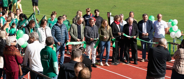 Viele Leute stehen auf einer Laufbahn und halten ein Absperrband in der Hand