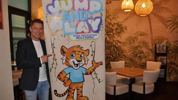 Ein Mann zeigt auf ein Plakat mit der Aufschrift „Jump and Play“