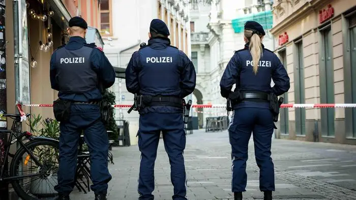 Das Bild zeigt Polizeibeamtinnen und -beamte auf der Straße vor einem Absperrband