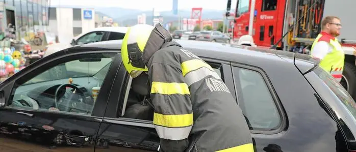 Ein Feuerwehrmann steht gebückt neben einem schwarzen Auto