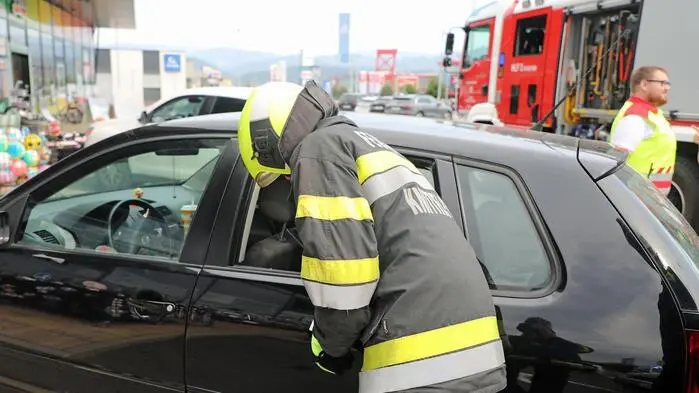 Ein Feuerwehrmann steht gebückt neben einem schwarzen Auto