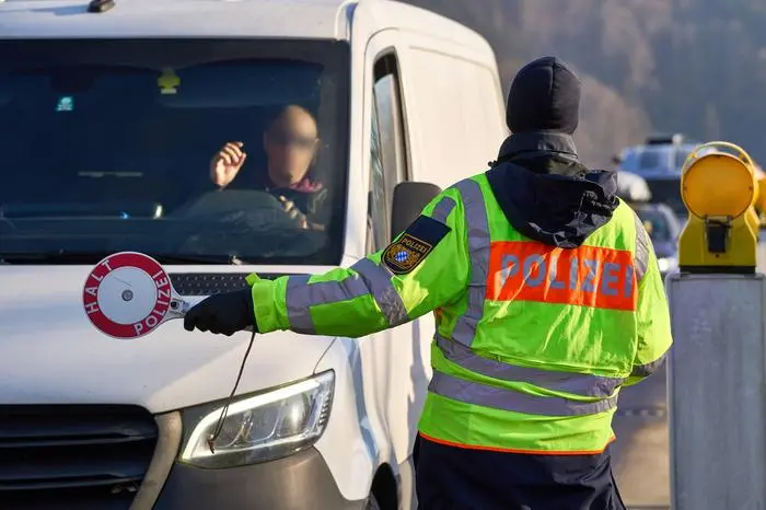 Oberaudorf, Bavaria, Germany - February 6, 2025: Symbolic image border control or traffic control. Policeman holding a police trowel with inscription: Halt police, in front of a vehicle at the border crossing from Austria to Germany *** Symbolbild Grenzkontrolle bzw. Verkehrskontrolle. Polizist hält eine Polizeikelle mit Aufschrift: Halt Polizei, vor ein Fahrzeug am Grenzübergang von Österreich nach Deutschland