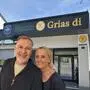 Ein Mann und eine Frau, beide Anfang 60, stehen vor einem Gebäude mit der Aufschrift „Grias di“