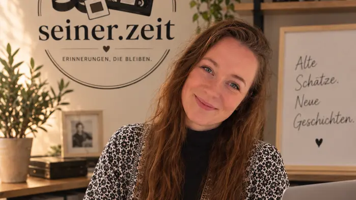 Eine Frau sitzt an einem Schreibtisch und lächelt in die Kamera.