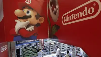 FILE - In this May 7, 2014 file photo, shoppers walk under the logo of Nintendo and Super Mario characters at an electronics store in Tokyo. Nintendo Co. reported Thursday, May 7, 2015 a net profit of 41.8 billion yen ($350 million) for the fiscal year through March, a reversal from deep losses the previous year, as it reshapes its troubled business with an unprecedented foray into smartphone games.  (AP Photo/Shizuo Kambayashi, File)