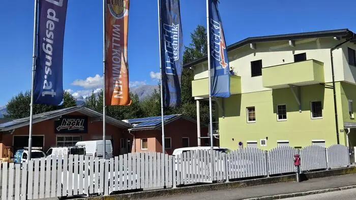 Grünes Gebäude, in dem sich das Café Piccolo befand. Davor wehen Firmenfahnen.
