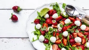 Plate of vegetarian summer salad with lime, arugula, strawberries, mozzarella, mint and daisies SARF04600 