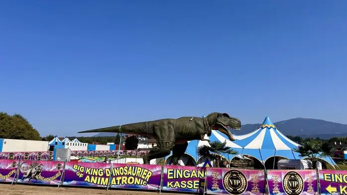 Ein großer Dinosaurier aus Plastik vor einer niedrigen Absperrung mit Werbeplakaten für die Ausstellung 