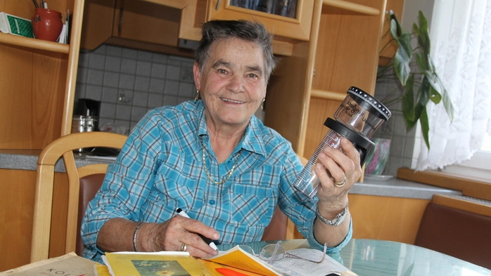 Eine ältere Dame mit einem blau-karierten Hemd hält einen Messbecher in der Hand 