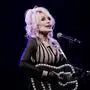 Dolly Parton spielt auf einer schwarzen Gitarre und singt in ein Mikrofon