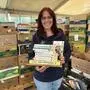 Eine Frau steht vor zahlreichen Bananenschachteln und hält mehrere Bücher in der Hand