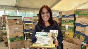 Eine Frau steht vor zahlreichen Bananenschachteln und hält mehrere Bücher in der Hand