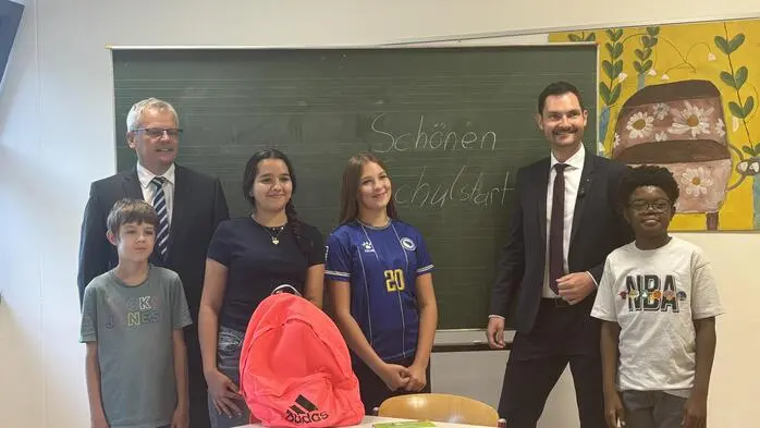 Zwei Erwachsene mit vier Schülern vor einer Schultafel