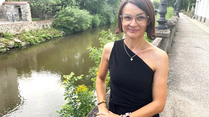 Zu sehen ist eine Frau mit kinnlagen braunen Haaren. Im Hintergrund ist ein Fluss zu sehen