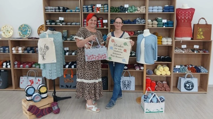 Zwei Damen stehen nebeneinander. Dahinter sind Handarbeitssachen zu sehen 