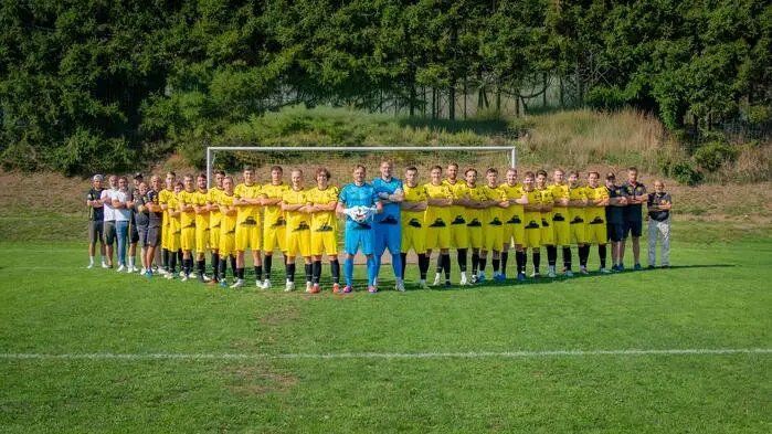 Eine Fußballmannschaft stellt sich für ein Foto auf. Die Spieler tragen gelbe Trikots.