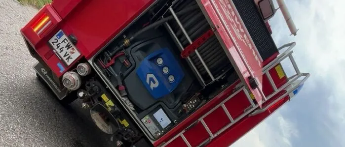 Zu sehen ist ein Feuerwehrauto daneben hockt ein Mann