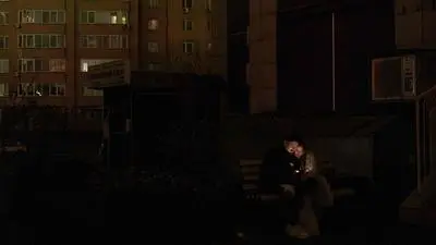 TOPSHOT - Local residents sit on a bench with smartphones on a non-illuminated street during blackout hours in Kyiv on December 10, 2025, following Russian missile and drone attacks on Ukrainian energy infrastructure amid the Russian invasion of Ukraine. Power outages are frequent across the country, as a result of both rolling blackouts imposed by the authorities to ration electricity and emergency outages triggered by hits to the energy network. (Photo by Roman PILIPEY / AFP)