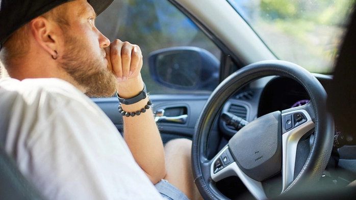 Ein Mann sitzt gelangweilt im Auto im Stau