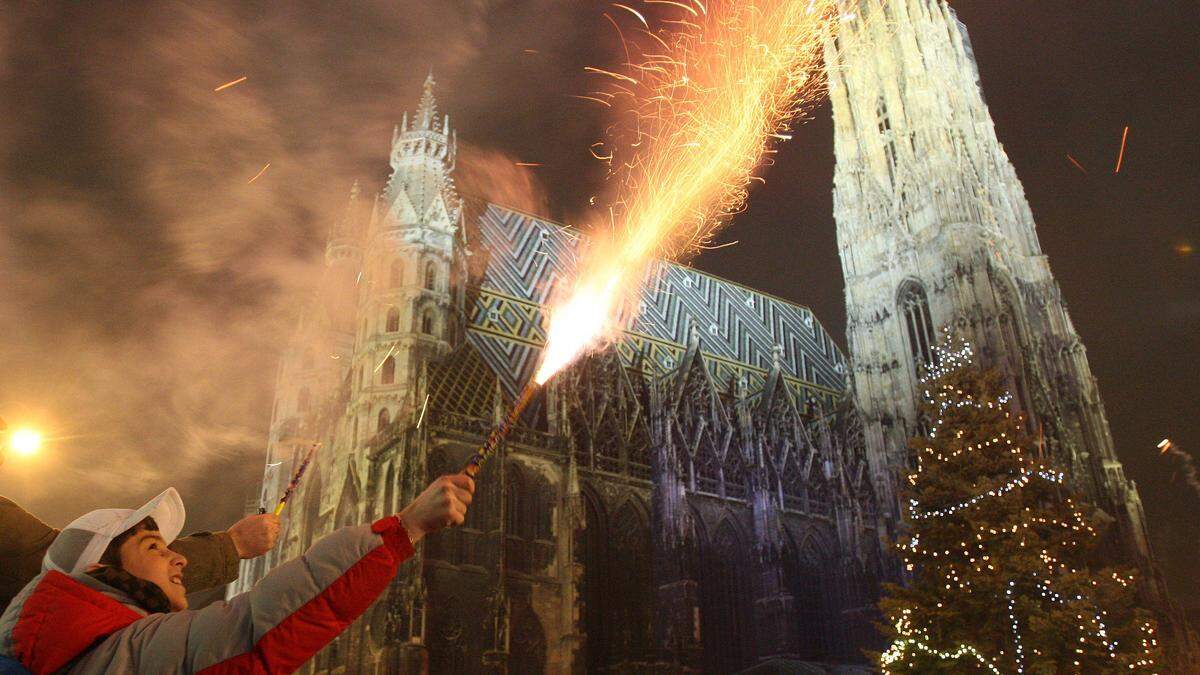 Ein Mann hält vor dem Wiener Stephansdom eine Sprühkerze in die Luft | Touristen aus aller Welt feiern traditionell in Wien Silvester