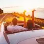 Happy Couple Driving on Country Road into the Sunset in Classic Vintage Sports Car 