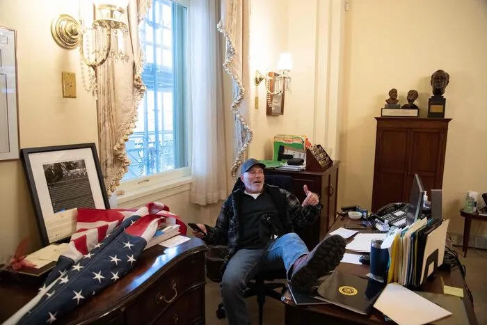 Während Jake Angeli sich in Szene setzte, drang Richard Barnett (60) in das Büro von Nancy Pelosi (80), der demokratischen Sprecherin des Repräsentantenhauses, ein und legte dort ganz gemütlich die Füße auf den Tisch.  Auch Barnett war als Trump-Anhänger bekannt. 