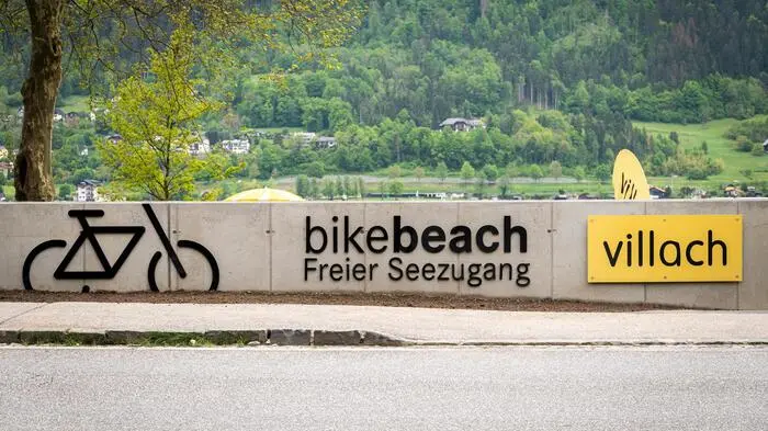 Eine Mauer vor einem See auf der „bikebeach Freier Seezugang“ geschrieben steht