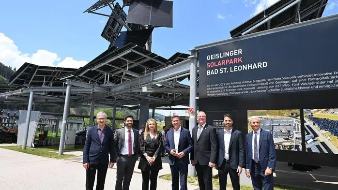 Mehrere Menschen stehen nebeneinander und lachen in die Kamera, dahinter die Solaranlage
