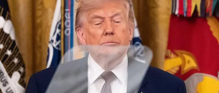 Donald Trump blickt Richtung Teleprompter. Hinter ihm sind Flaggen.