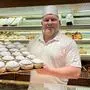 Ein Bäcker steht hinter dem Verkaufstresen und hält ein Blech voll mit Krapfen in die Kamera | Christian Berger von der Bäckerei Berger in Villach hat laut Falstaff-Voting die beliebtesten Krapfen Kärntens