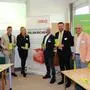 Eine Gruppe, bestehend aus Männern und Frauen in Business-Kleidung, steht in einem gut belichteten Raum