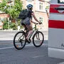 Sujetbild: Rechts im Bild ist die offene Autotür eines Rettungswagens zu sehen, links fährt eine Radfahrerin mit Helm und Rucksack vorbei