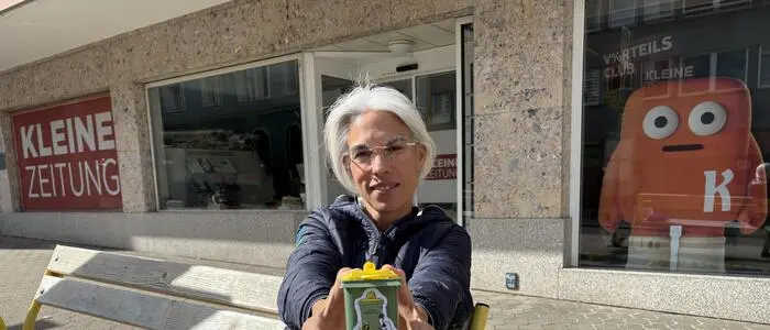 Eine Frau mit Brille sitzt auf einer Bank und hält eine kleine Mülltonne in den Händen