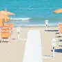 Strand mit orangefarbenen Sonnenschirmen und Liegen vor türkisblauem Meer