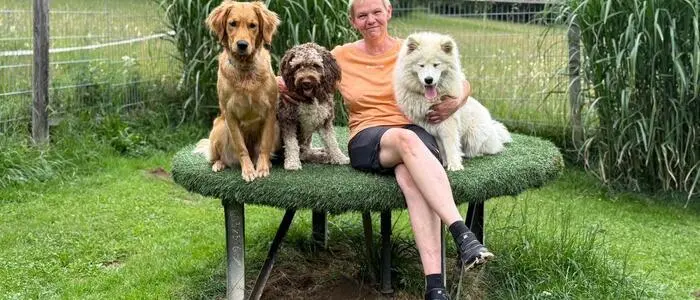 Eine Frau sitzt mit drei Hunden auf einem Hocker