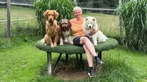 Eine Frau sitzt mit drei Hunden auf einem Hocker