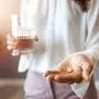 Close up photo of one round white pill in young female hand. Woman takes medicines with glass of water. Daily norm of vitamins, effective drugs, modern pharmacy for body and mental health concept